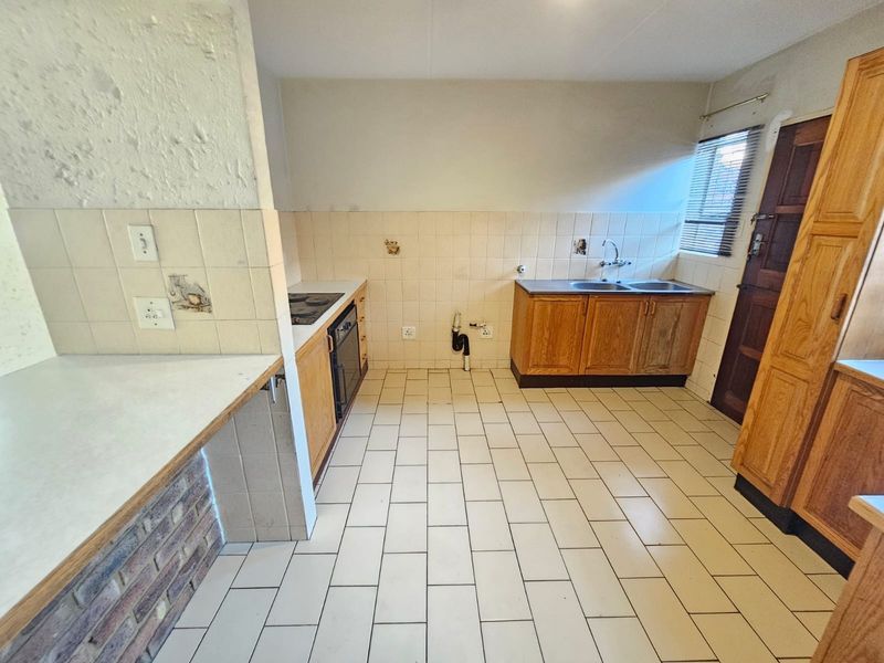A dated kitchen featuring wooden cabinetry, a double basin sink, built-in oven, and tiled flooring, offering a blank canvas for renovation.