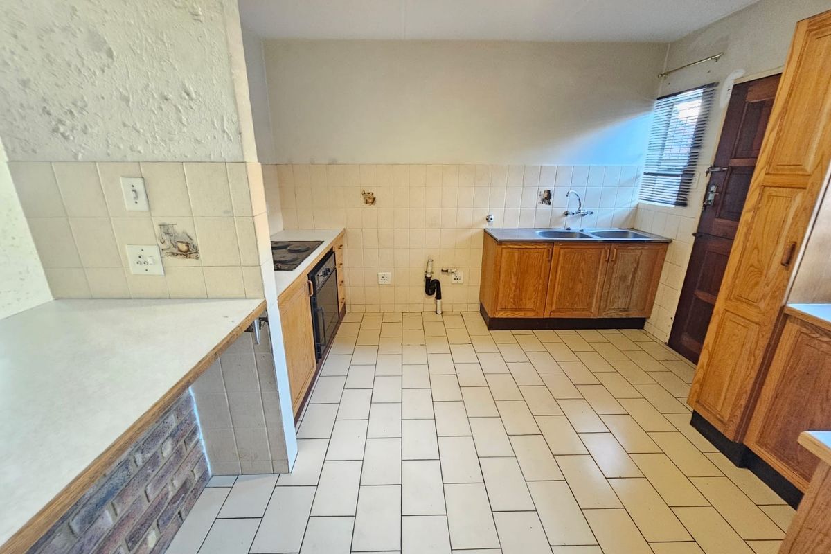 A dated kitchen featuring wooden cabinetry, a double basin sink, built-in oven, and tiled flooring, offering a blank canvas for renovation.