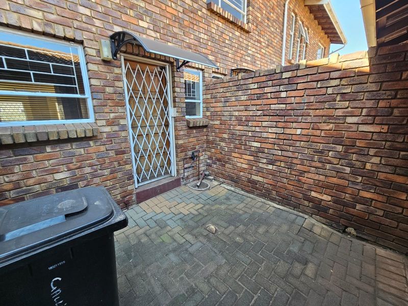 A private rear courtyard featuring brick walls, paved flooring, and a secure entrance door with an overhead awning.