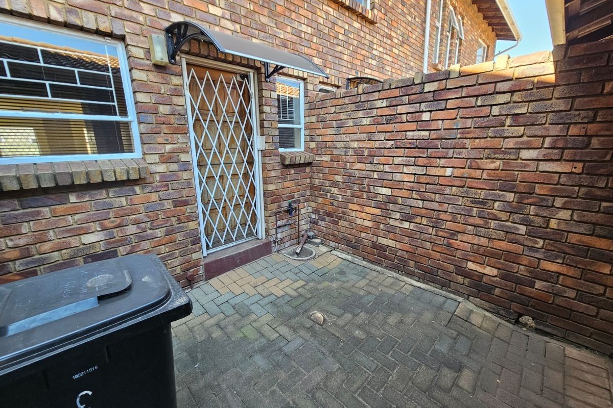 A private rear courtyard featuring brick walls, paved flooring, and a secure entrance door with an overhead awning.