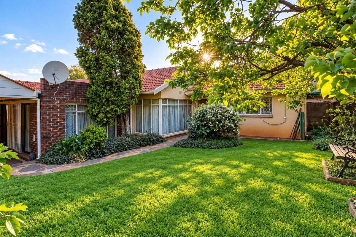 A well-maintained rear garden featuring a lush lawn, mature trees, paved pathways, and a classic brick and tile exterior facade.
