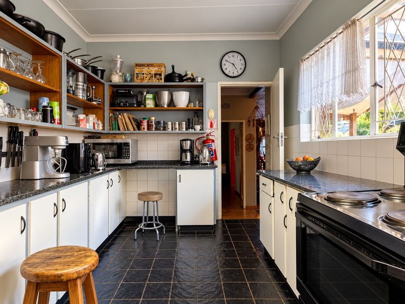 A functional kitchen featuring built-in cabinetry, laminate countertops, tiled backsplash, and an electric stove, with open shelving for storage.
