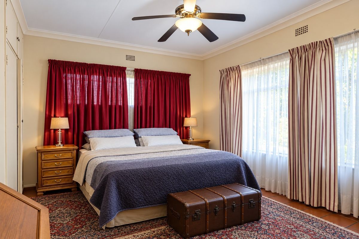 A well-maintained bedroom featuring a ceiling fan, built-in wardrobe, and large windows with classic drapery, offering a comfortable and functional living space.