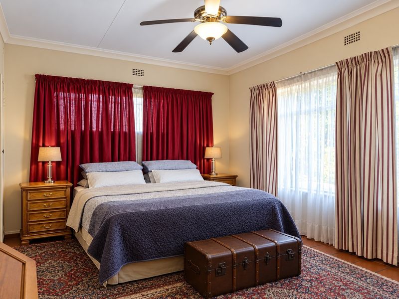 A well-maintained bedroom featuring a ceiling fan, built-in wardrobe, and large windows with classic drapery, offering a comfortable and functional living space.