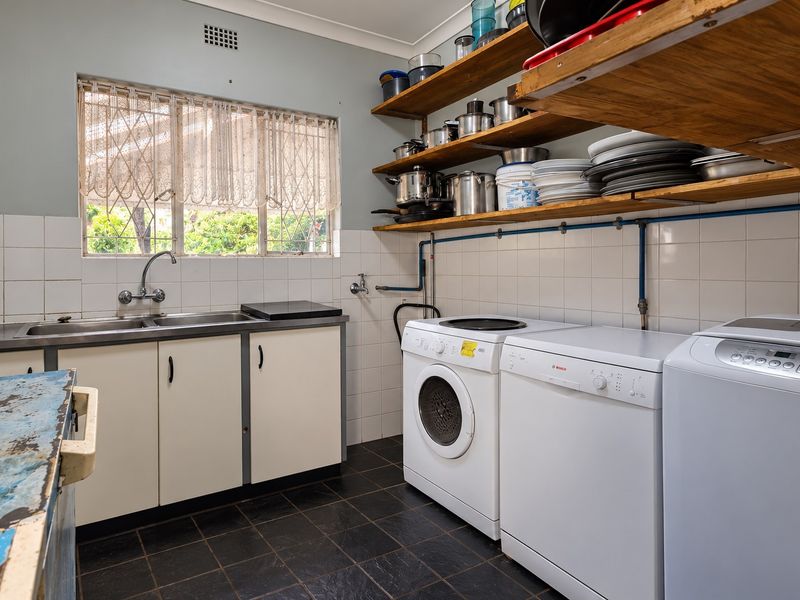 Functional laundry room featuring a double stainless steel sink, tiled splashback, open timber shelving, and dedicated plumbing connections for laundry appliances.
