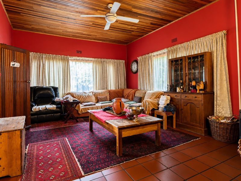 A cozy living room featuring a warm timber-clad ceiling, ceiling fan, terracotta-style tiled flooring, and a built-in wood-burning fireplace.