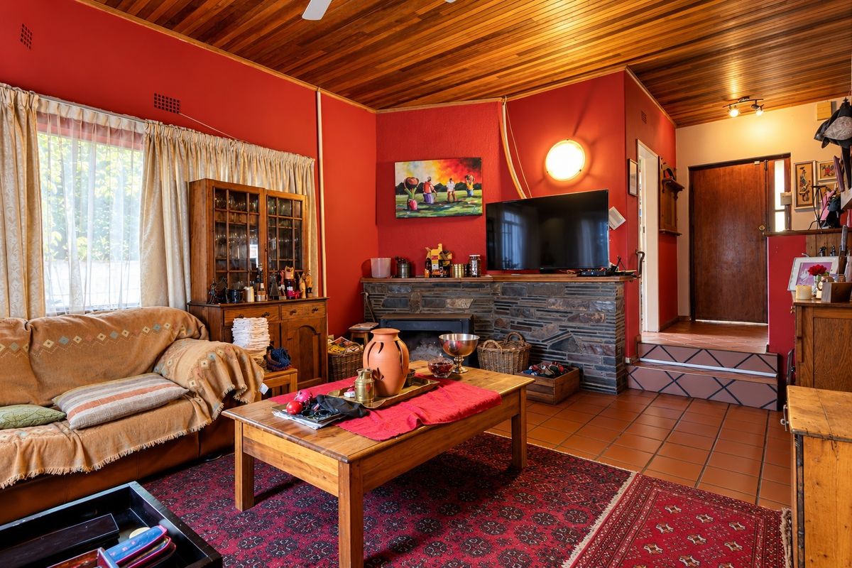 A living room featuring a stone fireplace, wood-paneled ceiling, and terracotta tiled flooring with a raised step area leading to an entrance.