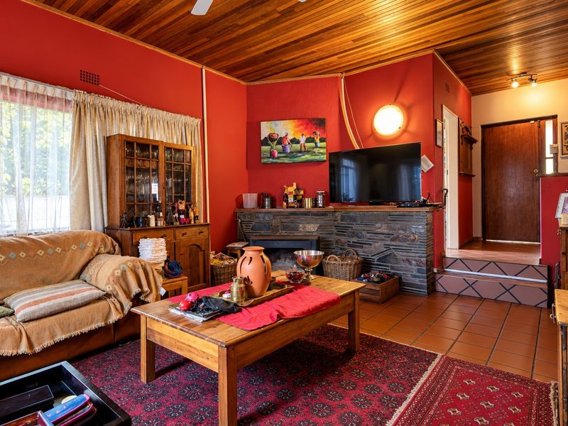 A living room featuring a stone fireplace, wood-paneled ceiling, and terracotta tiled flooring with a raised step area leading to an entrance.