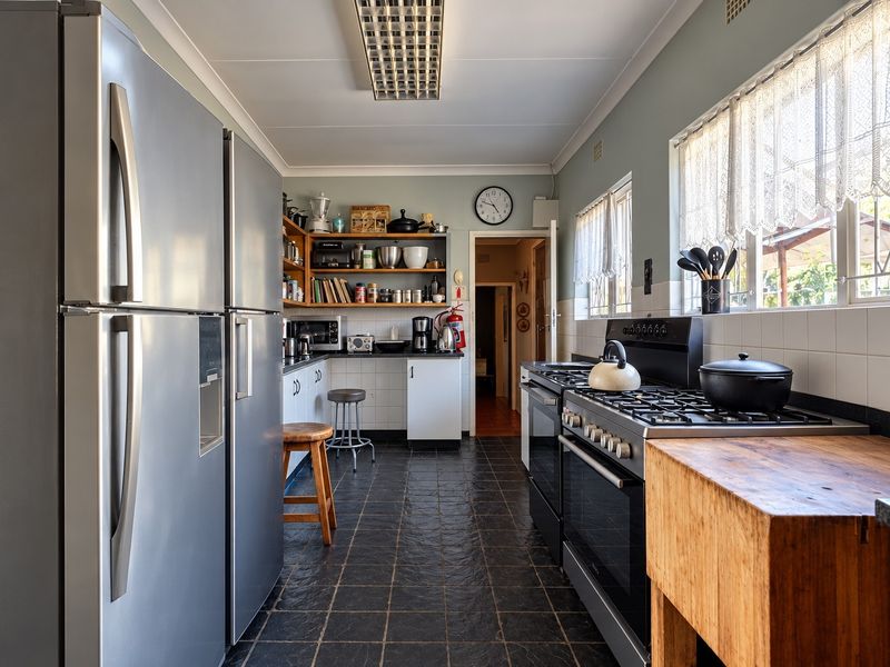 A functional kitchen featuring a gas stove, tiled backsplash, and ample built-in cabinetry with dark tiled flooring.
