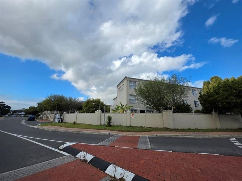 Exterior view of the apartment complex featuring a perimeter wall with electric fencing and paved street access.