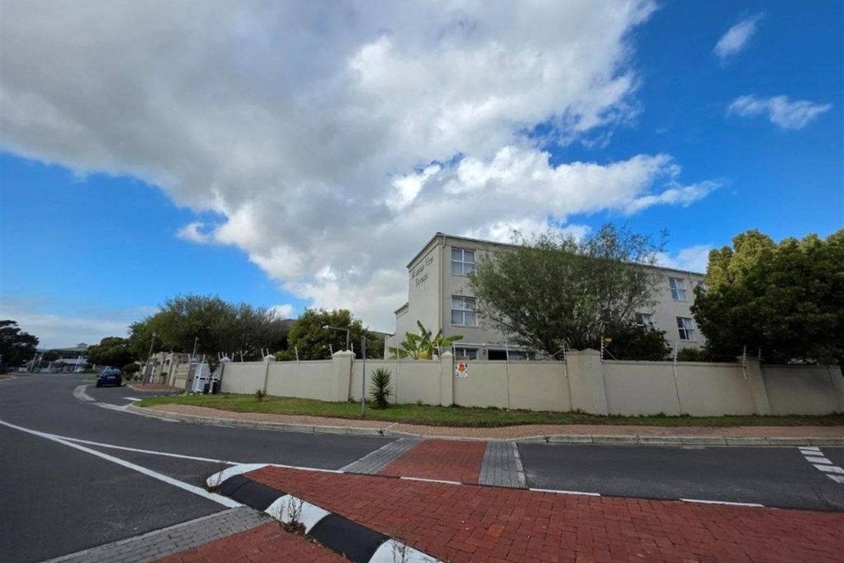 Exterior view of the apartment complex featuring a perimeter wall with electric fencing and paved street access.