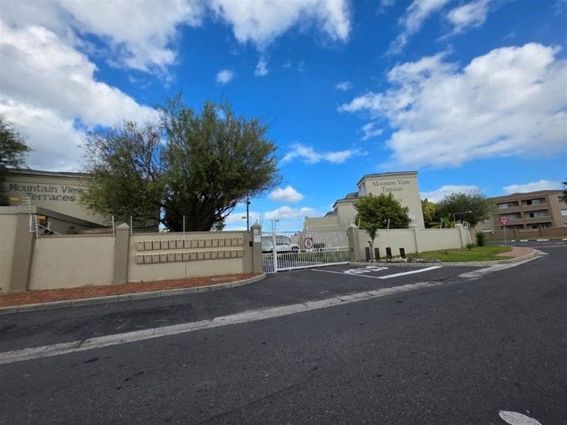 Street view of the Mountain View Terraces apartment complex entrance, featuring a secure perimeter wall, electric fencing, and a bank of mailboxes.