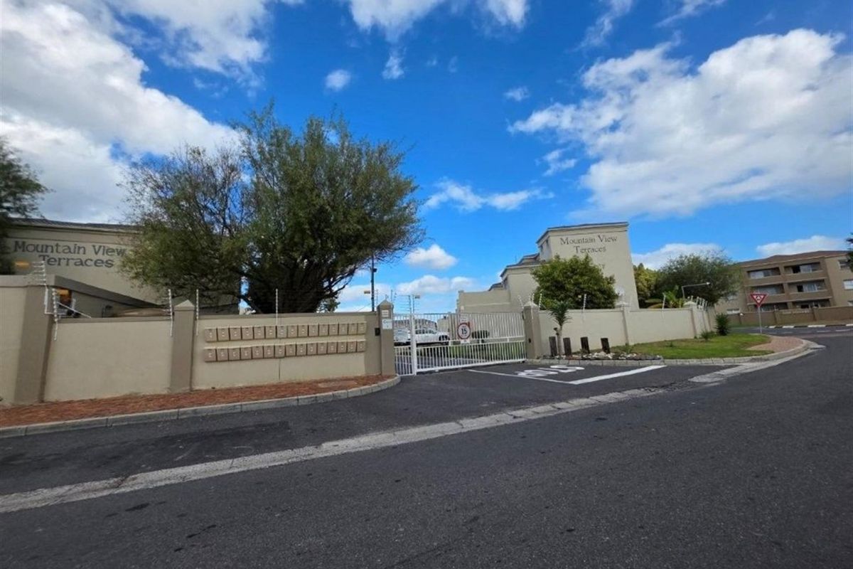 Street view of the Mountain View Terraces apartment complex entrance, featuring a secure perimeter wall, electric fencing, and a bank of mailboxes.