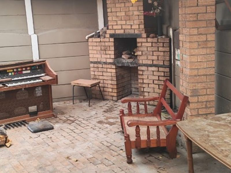 Covered outdoor patio area featuring a traditional brick built-in braai, brick paving, and exposed timber roof structure.