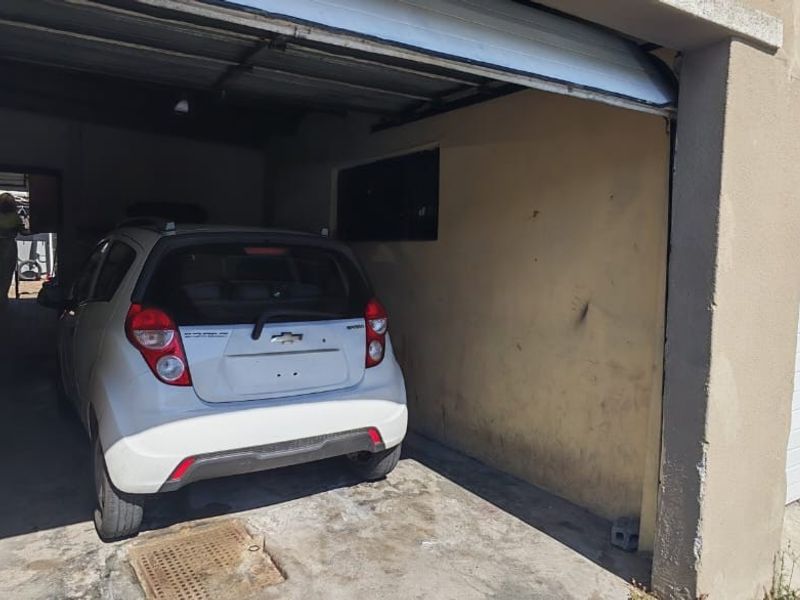 A functional single-car garage featuring a roll-up door, concrete flooring, and integrated drainage, showing signs of wear on the walls and floor.