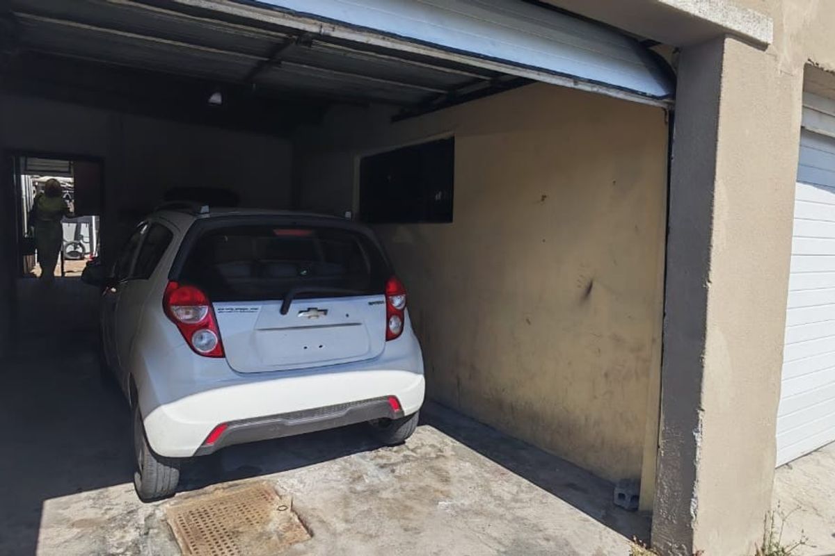 A functional single-car garage featuring a roll-up door, concrete flooring, and integrated drainage, showing signs of wear on the walls and floor.