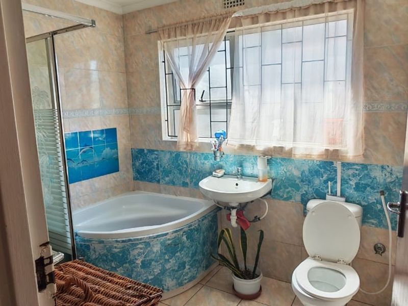 A functional bathroom featuring a corner bathtub, shower enclosure, wall-mounted basin, and toilet with dated decorative wall tiling.
