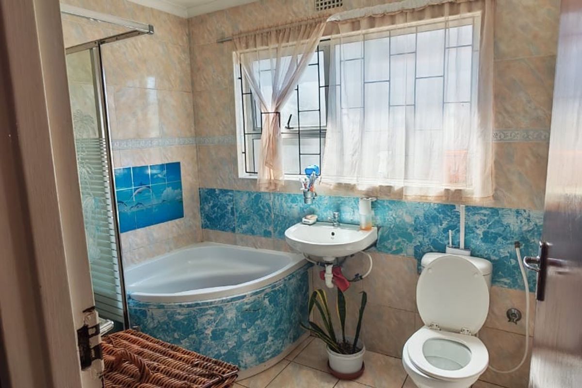 A functional bathroom featuring a corner bathtub, shower enclosure, wall-mounted basin, and toilet with dated decorative wall tiling.