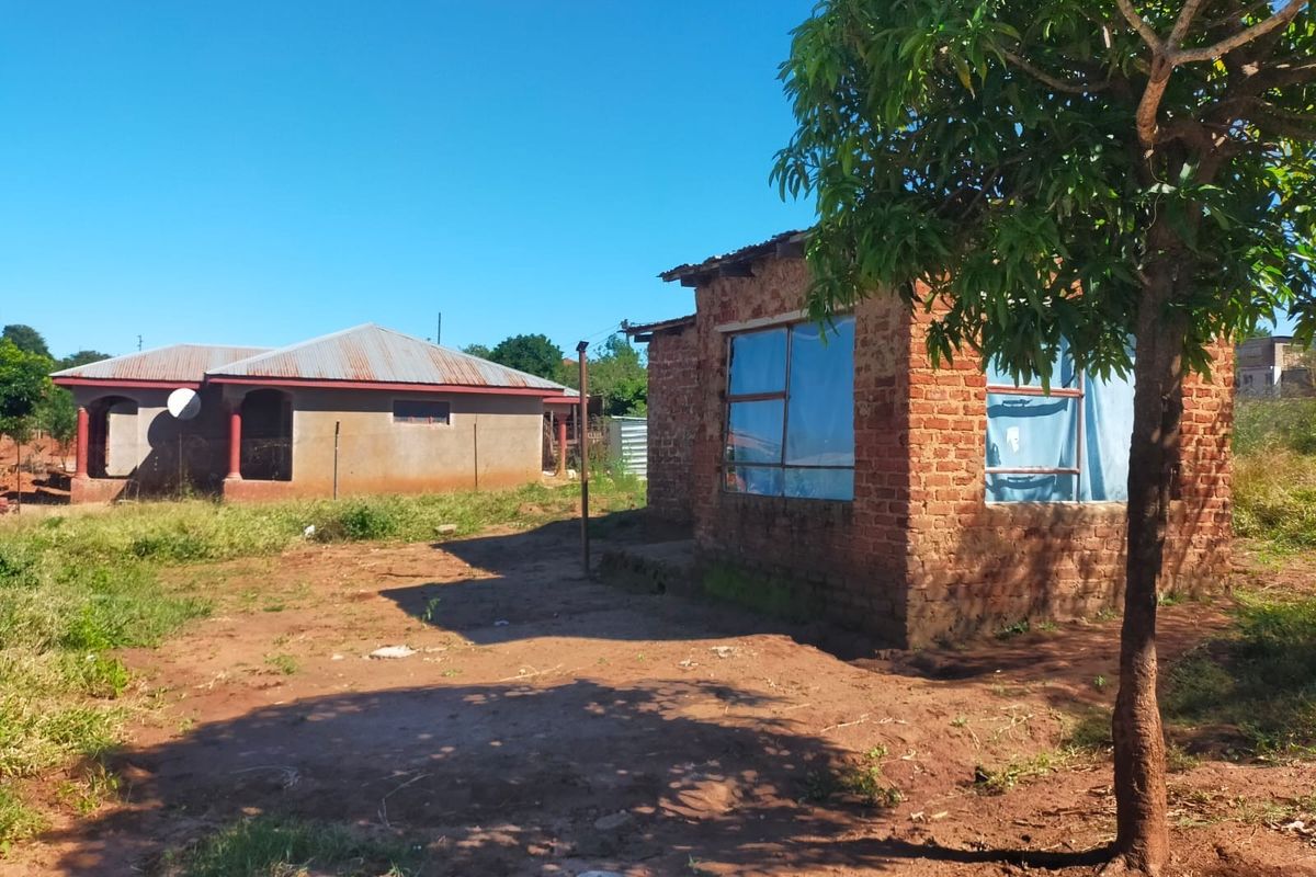 View of a residential property featuring an exposed brick structure with a corrugated metal roof and an unpaved yard area.