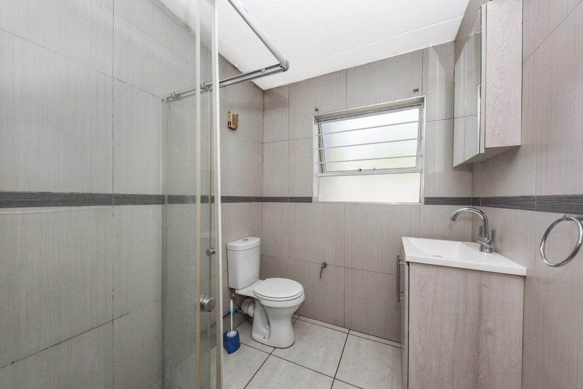A functional bathroom featuring a shower enclosure, toilet, and vanity cabinet with a basin, finished with neutral wall and floor tiling.