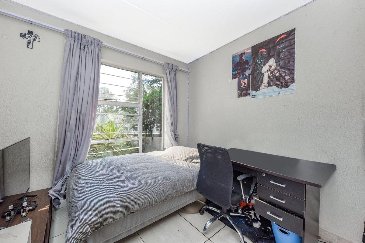 A compact bedroom featuring tiled flooring and a large window with security bars, providing natural light and garden views.