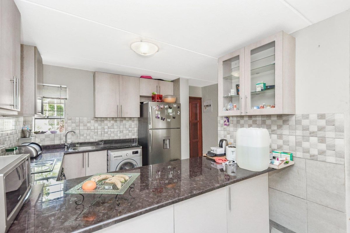 A functional kitchen featuring granite countertops, ample built-in cabinetry, a tiled backsplash, and an integrated washing machine.
