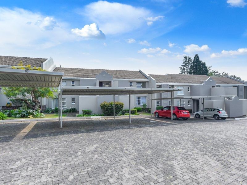 Exterior view of an apartment complex featuring covered parking bays and a paved driveway area.