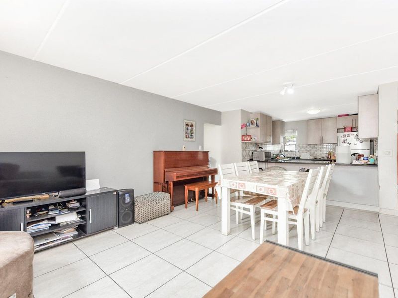Open-plan living and dining area featuring tiled flooring and a functional kitchen with built-in cabinetry and tiled backsplash.