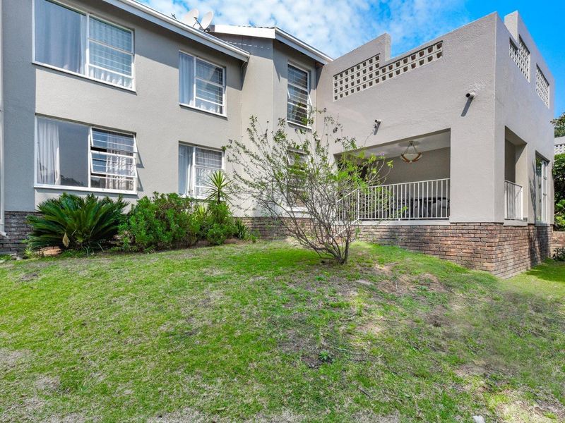 Rear view of the apartment building featuring a covered patio, brick base detailing, and a landscaped garden area.