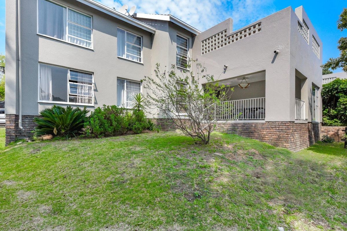 Rear view of the apartment building featuring a covered patio, brick base detailing, and a landscaped garden area.