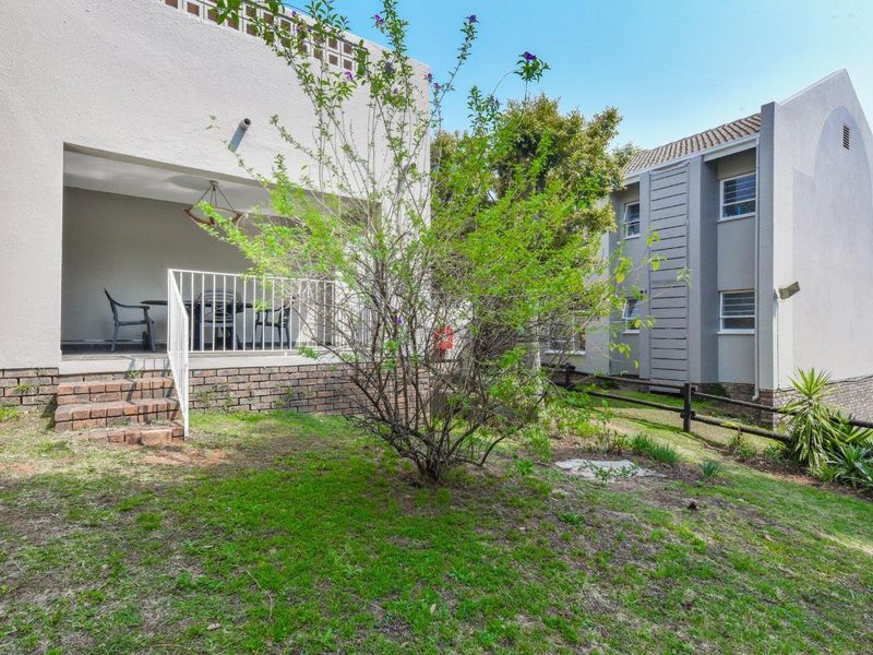Rear view of the apartment building featuring a covered patio, brick retaining wall, and a small private garden area.