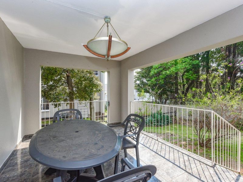 A covered patio featuring tiled flooring and a metal balustrade, overlooking a lush garden area.