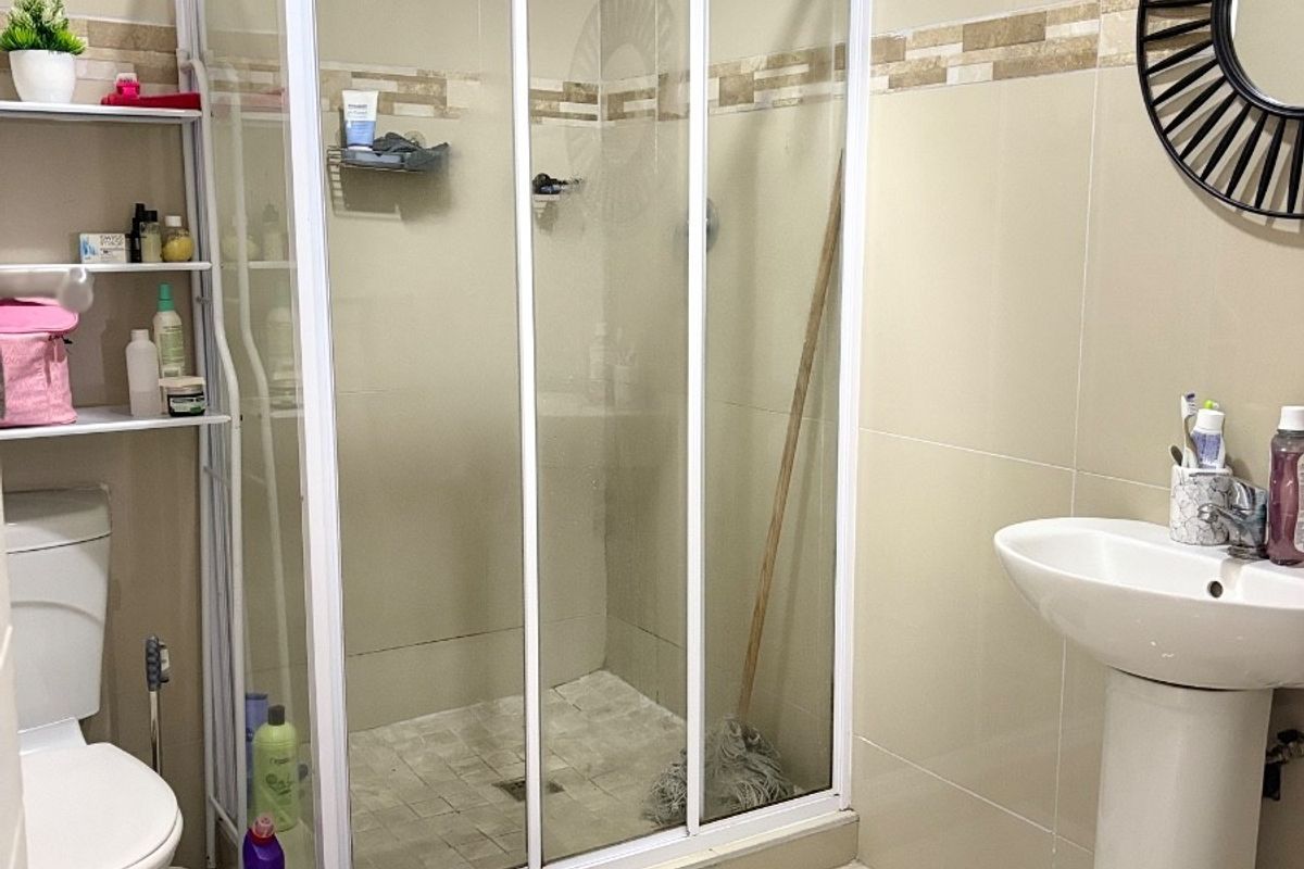 A functional bathroom featuring a shower enclosure, pedestal basin, and toilet with neutral wall and floor tiling.