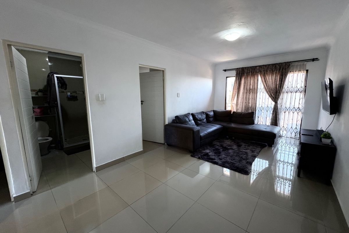 A bright living room featuring neutral tiled flooring, a sliding door with security gate, and direct access to an adjacent bathroom.