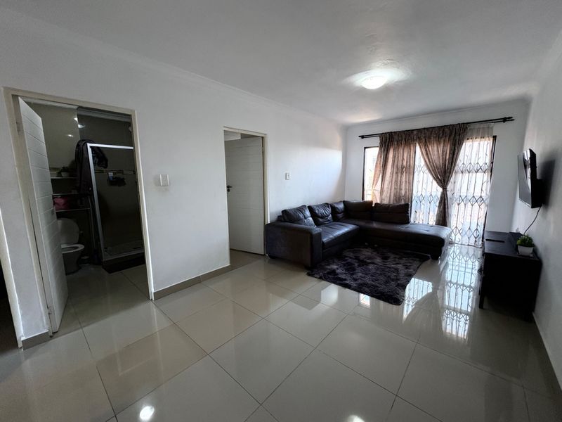 A bright living room featuring neutral tiled flooring, a sliding door with security gate, and direct access to an adjacent bathroom.