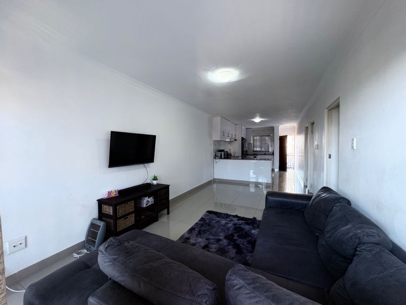Open-plan living area featuring tiled floors and a functional kitchen with built-in cabinetry, creating a seamless flow between the lounge and cooking space.