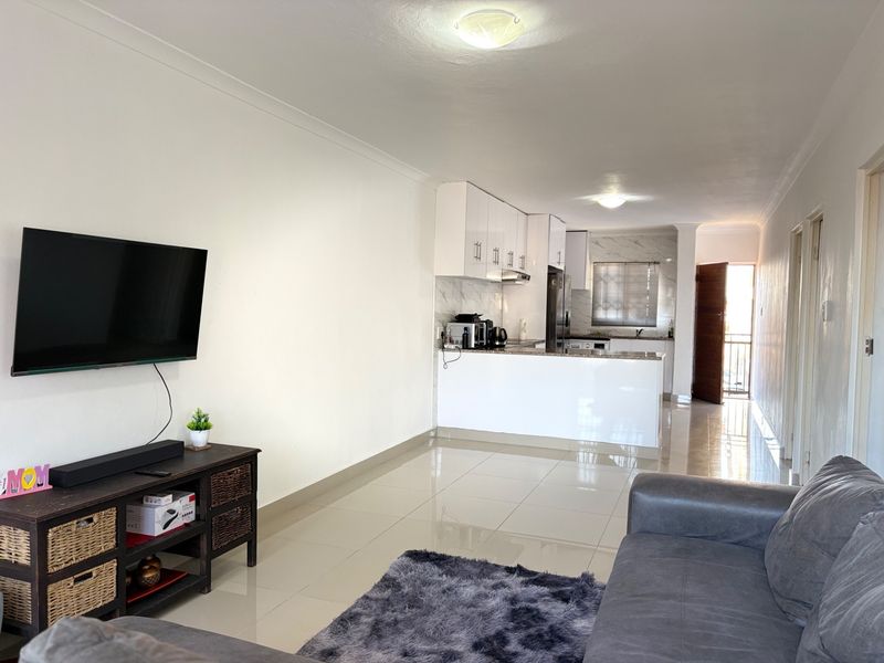 Open-plan living area featuring tiled floors and a modern kitchen with white cabinetry and granite countertops, leading to an exterior entrance.
