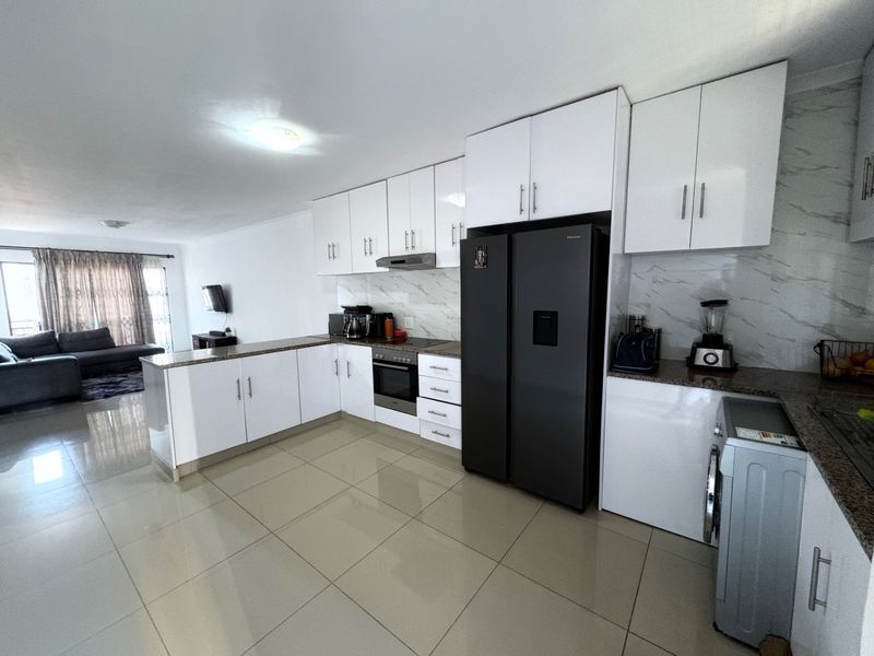 Modern open-plan kitchen featuring white high-gloss cabinetry, granite countertops, marble-look splashbacks, and integrated appliances, flowing seamlessly into the living area.