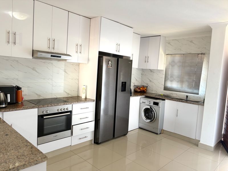 Modern kitchen featuring white cabinetry, granite countertops, marble-look backsplash, integrated appliances, and tiled flooring.