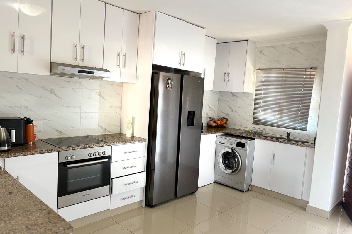 Modern kitchen featuring white cabinetry, granite countertops, marble-look backsplash, integrated appliances, and tiled flooring.
