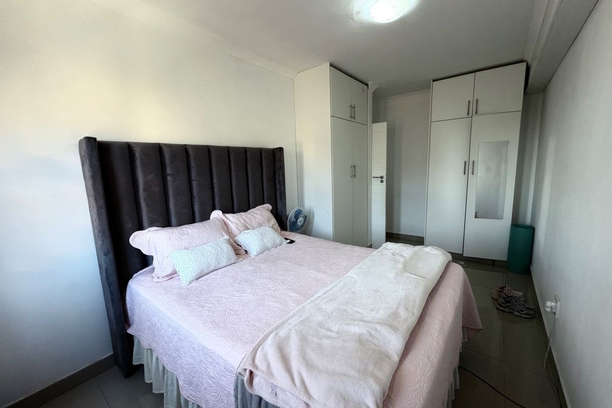 A well-maintained bedroom featuring built-in cupboards, neutral tiled flooring, and a central ceiling light fixture.