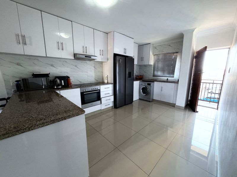 Modern kitchen featuring white cabinetry, granite countertops, marble-look splashback, built-in oven, hob, and tiled flooring with direct access to a balcony.