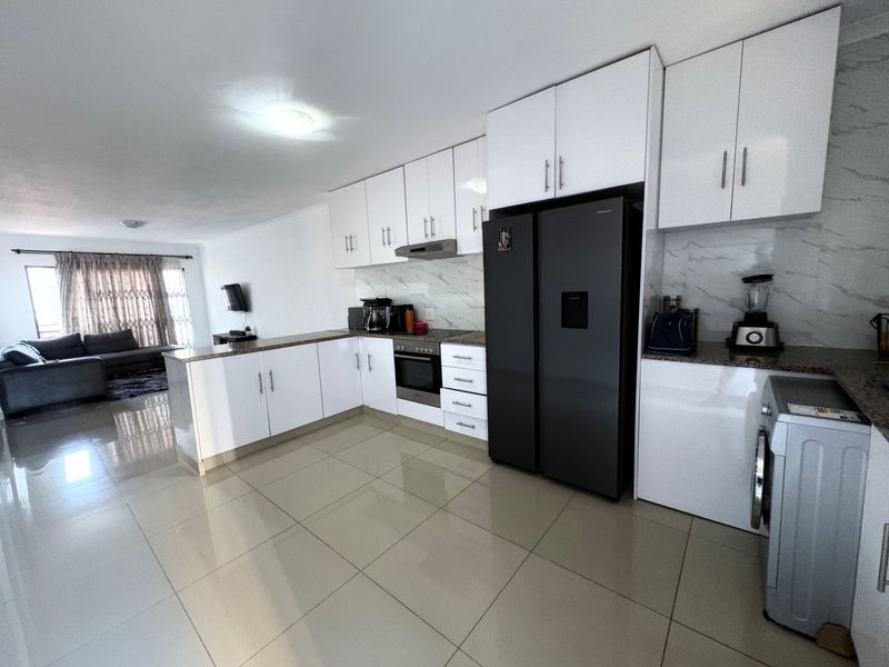 Modern open-plan kitchen featuring glossy white cabinetry, granite countertops, and marble-look splashback, seamlessly flowing into the adjacent living area.