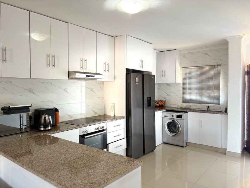 Modern kitchen featuring white cabinetry, granite countertops, marble-look backsplash, built-in oven, hob, extractor fan, and integrated space for laundry appliances.