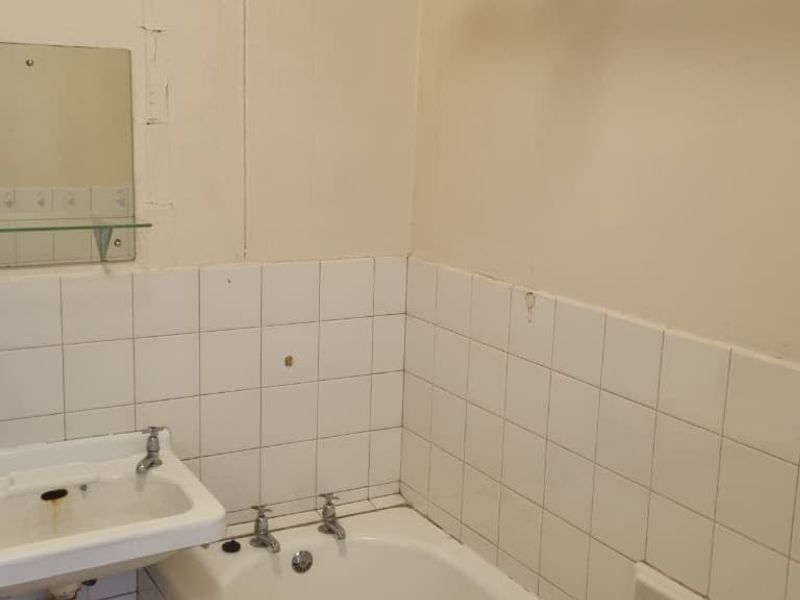A dated bathroom featuring a wall-mounted basin, bathtub, and tiled splashback, requiring significant renovation and cosmetic updates to improve its condition.