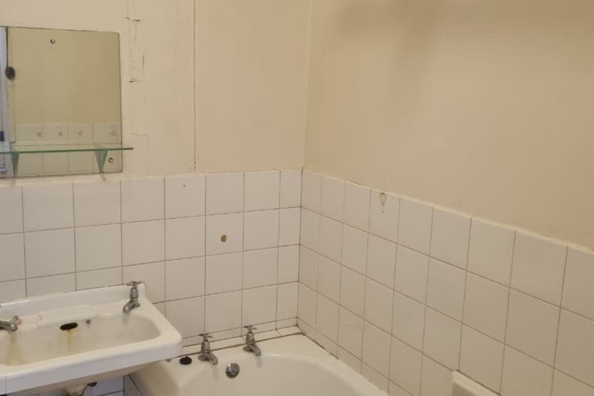 A dated bathroom featuring a wall-mounted basin, bathtub, and tiled splashback, requiring significant renovation and cosmetic updates to improve its condition.