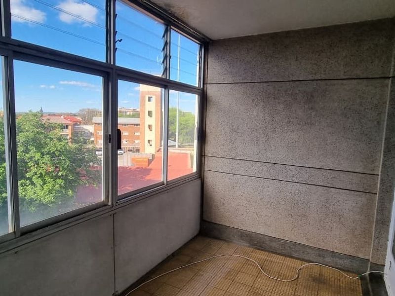 An enclosed balcony or sunroom featuring large louvre windows, tiled flooring, and textured wall finishes, offering an elevated view of the surrounding neighborhood.