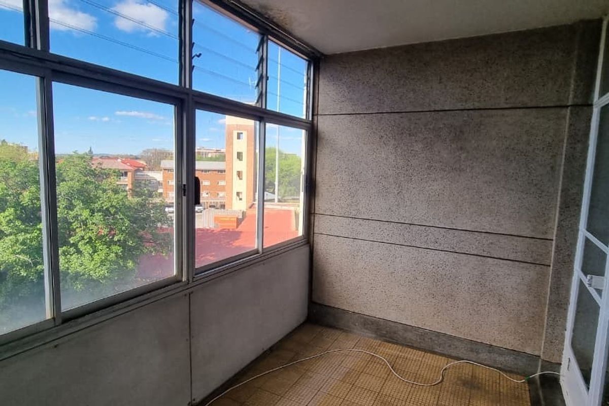 An enclosed balcony or sunroom featuring large louvre windows, tiled flooring, and textured wall finishes, offering an elevated view of the surrounding neighborhood.