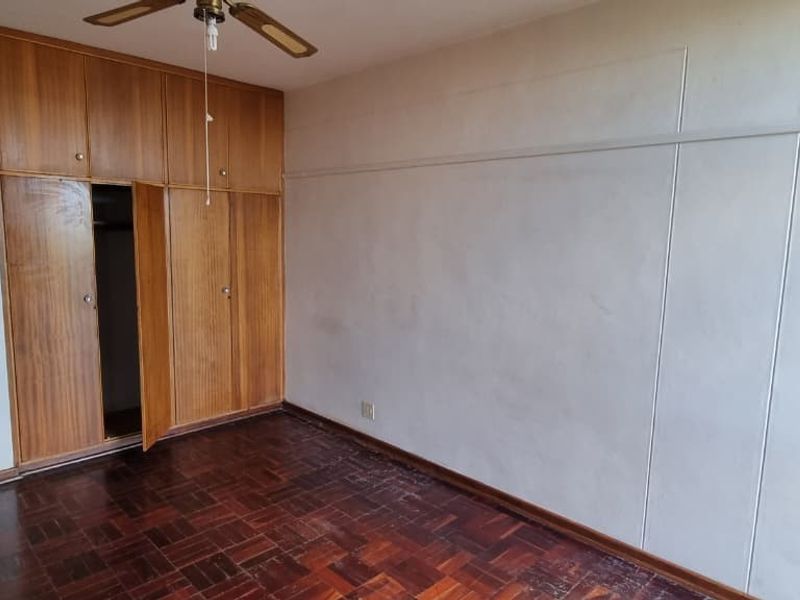 A vacant bedroom featuring original parquet flooring, built-in wooden cabinetry, and a ceiling fan, offering a blank canvas for renovation.