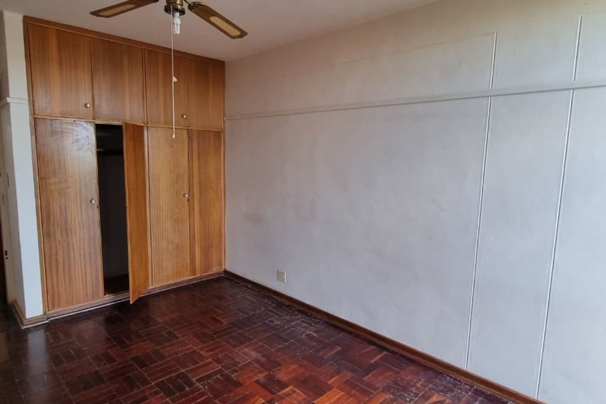 A vacant bedroom featuring original parquet flooring, built-in wooden cabinetry, and a ceiling fan, offering a blank canvas for renovation.